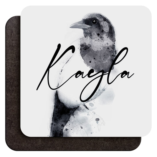 A 9 cm wood coffee coaster shown from both sides, with a watercolour magpie art print and custom cursive text saying ‘Kayla’ as an example on one side and dark wood backing on the other, shown against a white background